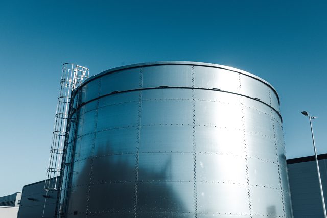 Metal industrial tank for water or fuel against blue sky.